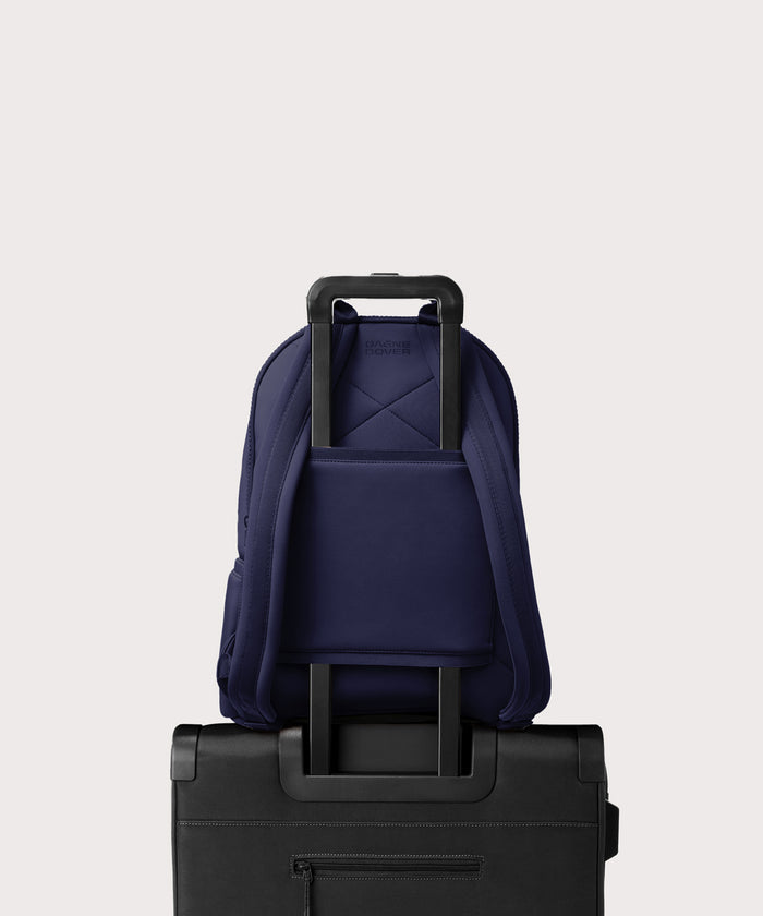 Dagne Dover large Dakota Neoprene Backpack in dark blue strapped to luggage with the neoprene luggage-handle sleeve.