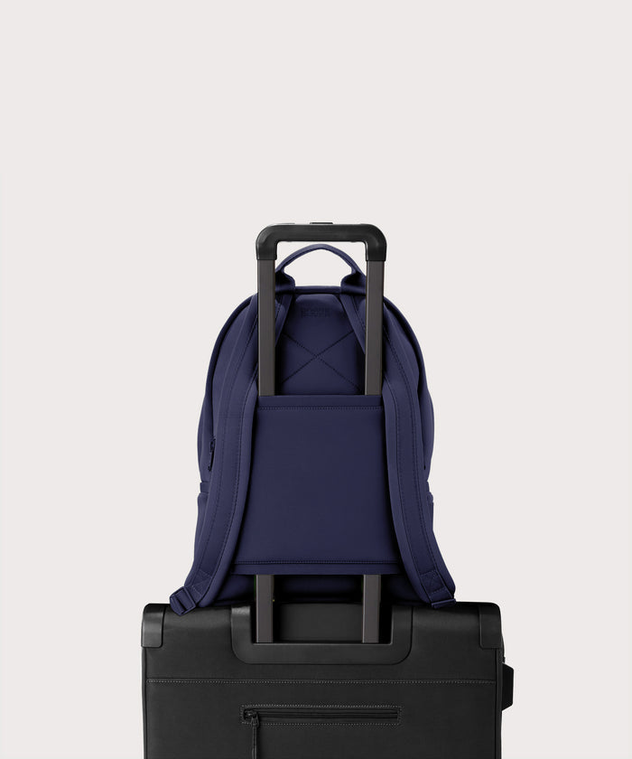 Dagne Dover medium Dakota Neoprene Backpack in dark blue strapped to luggage with the neoprene luggage-handle sleeve.